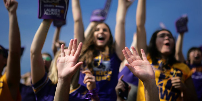 Close up of Laurier fans cheering with hands in the air in purple and gold attire