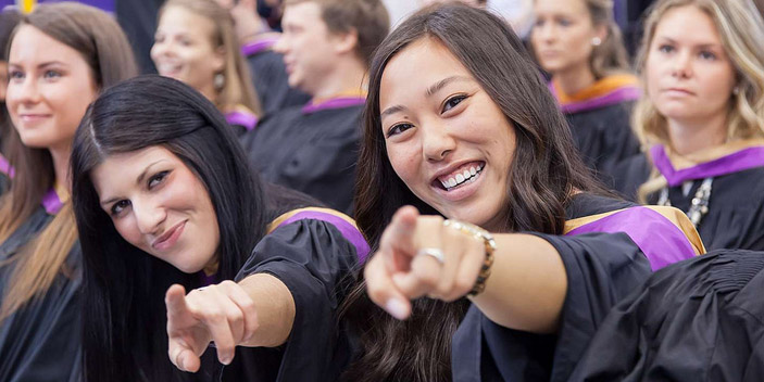 Zoom in of two graduates smiling and pointing at the camera