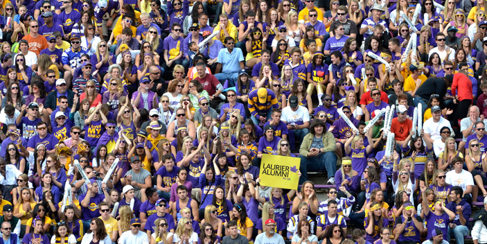 Wide view of laurier fans on bleachers at stadium cheering in laurier gear